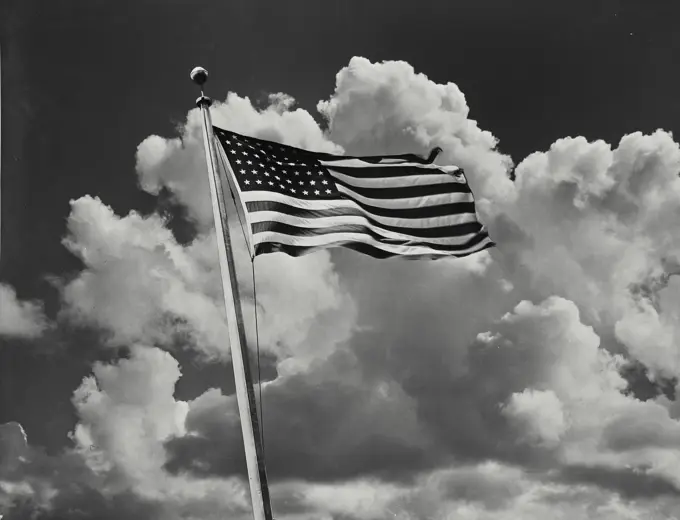 Vintage Photograph. View looking up at the American Flag with clouds behind