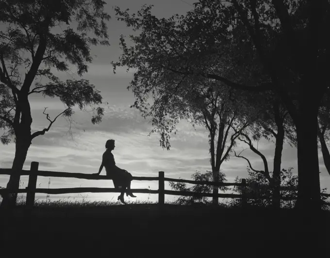 Vintage Photograph. Silhouette of girl sitting on rail fence.