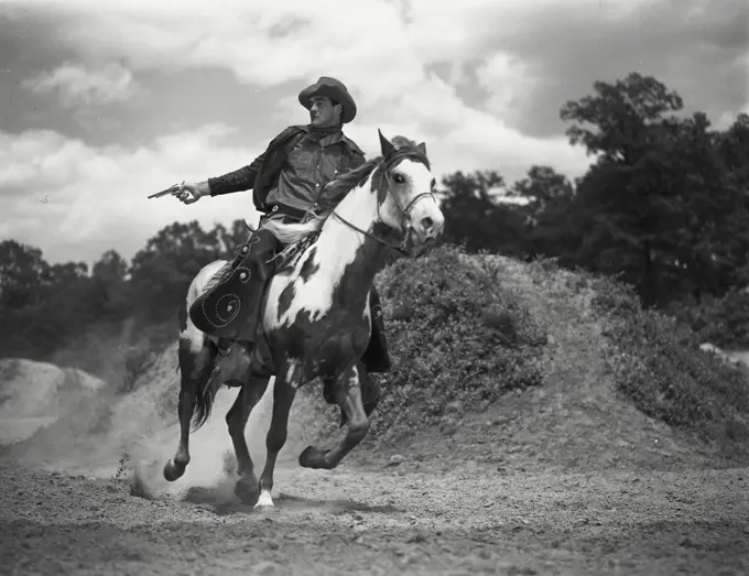 Vintage Photograph. Man in chaps riding on horses back shooting gun. Frame 2