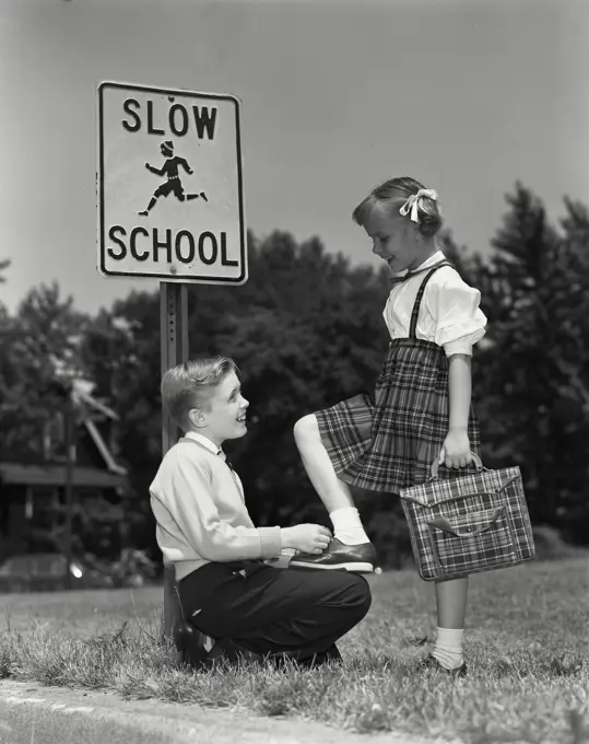 Vintage Photograph. Young boy tying young girls shoe at bus stop