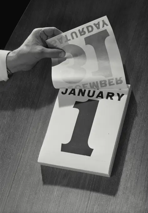 Vintage Photograph. Hand flipping up page of daily calendar from December 31st to January 1st, New Years Day, Frame 1