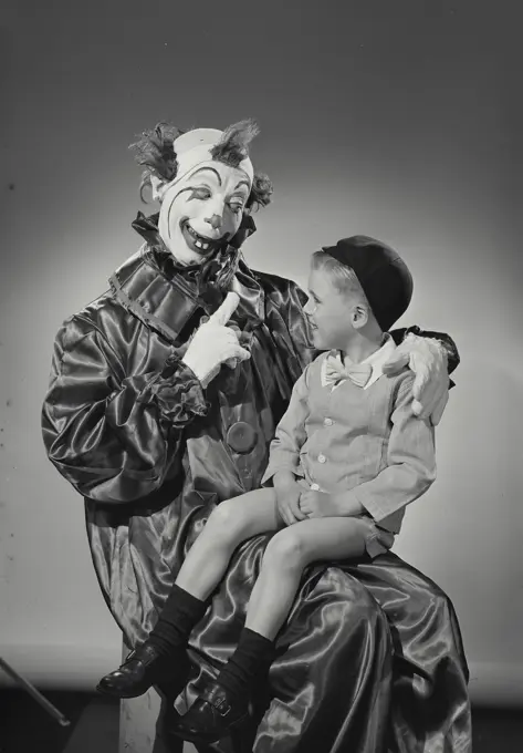 Vintage Photograph. Young boy sitting in lap of clown whose holding up hand with finger pointed