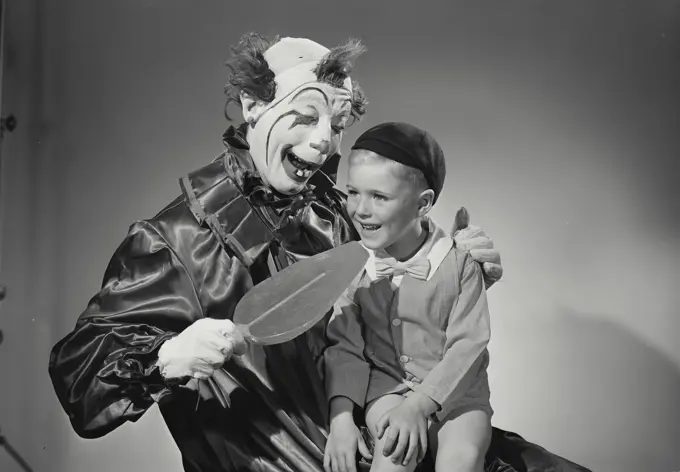 Vintage Photograph. Young boy sitting in lap of clown holding large oversized lollipop