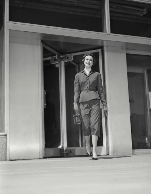 Vintage Photograph. Fashionable woman walking away from revolving doors of building