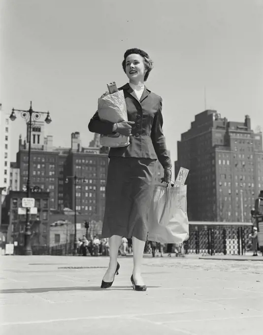 Vintage Photograph. Fashionable woman standing on sidewalk holding bags of groceries Frame 1
