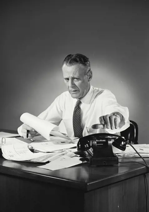 Vintage Photograph. Model Released. Man in button shirt and tie sitting at desk covered in papers. Frame 1