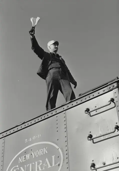 Vintage Photograph. Railroad brakement on top of freight car signaling with paper in hand, Frame 1