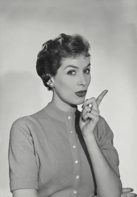 Vintage Photograph. Woman wearing button up sweater with hand raised pointing index finger and lips pursed