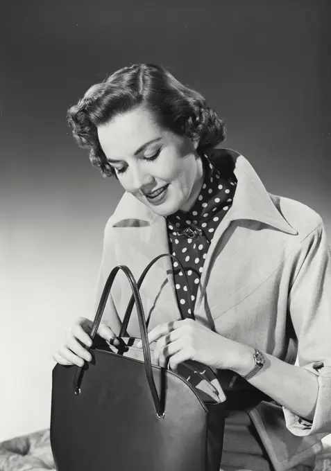 Vintage Photograph. Woman with curly hair wearing coat with wide collar over polka dot blouse looking in purse, Frame 1