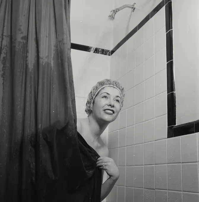 Vintage Photograph. Woman wearing shower cap peeking from behind shower curtain with water running behind her