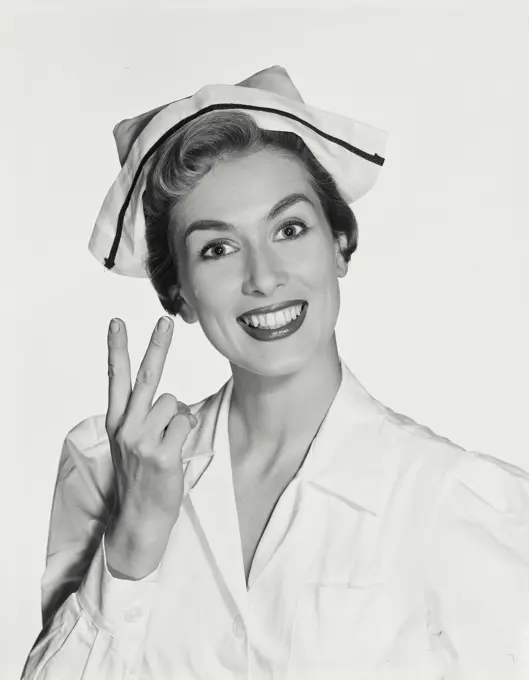 Vintage Photograph. Woman wearing nurse uniform smiling holding up two fingers on right hand