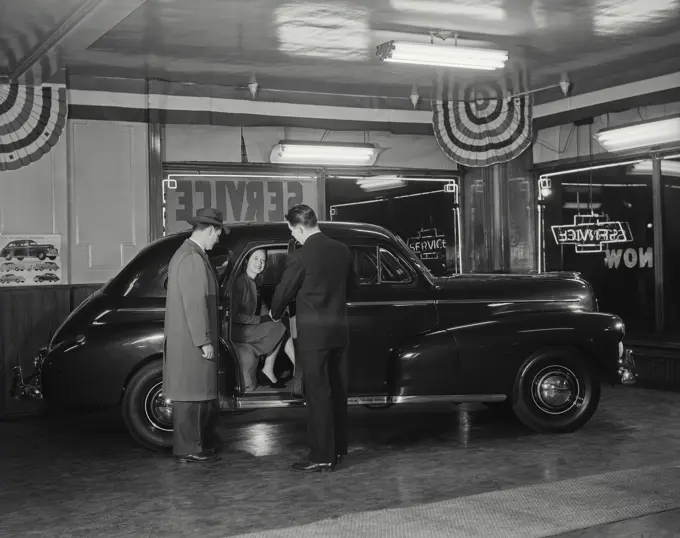 Vintage Photograph. Salesman showing new Chevrolet automobile to couple at dealership, woman sitting in backseat of car with door open, smiling, Frame 1