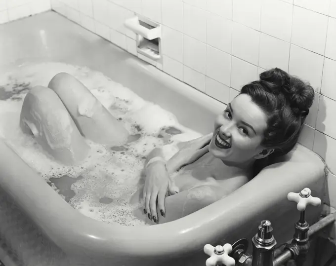 Vintage Photograph. Smiling brunette woman lying in sudsy bathtub looking up