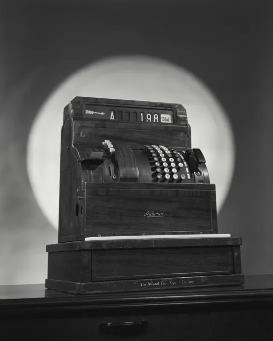 Vintage Photograph. National brand Cash register till on wooden desk with dramatic spotlight on background turned slightly to right, viewed from below