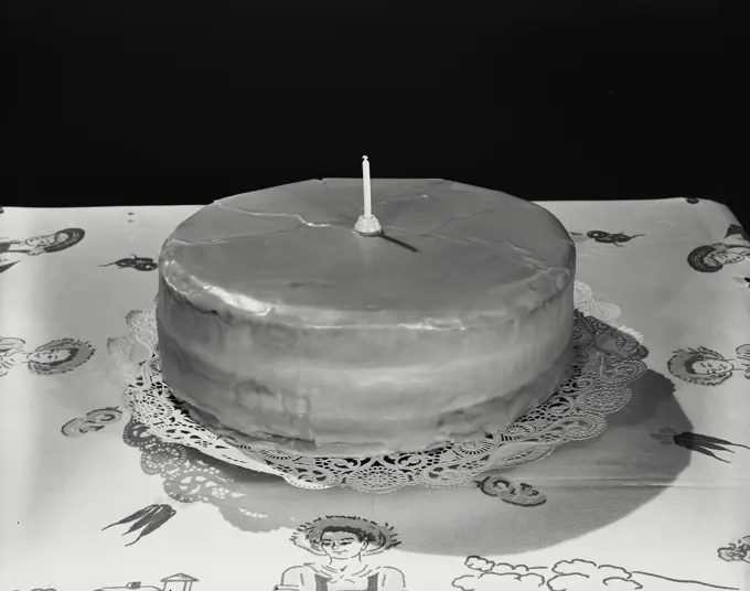 Vintage Photograph. Cake on lace doily with one candle on table with tablecloth