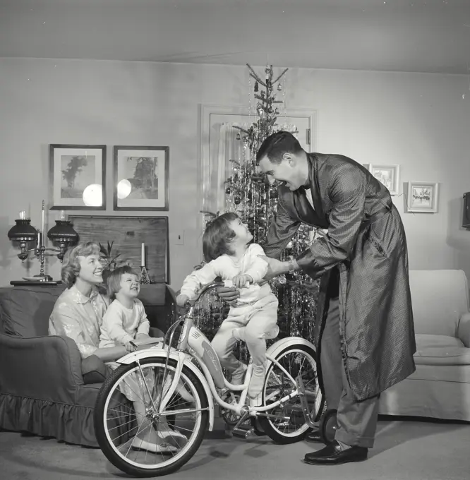 Vintage Photograph. Family gathered around Christmas tree father and child play with bicycle.