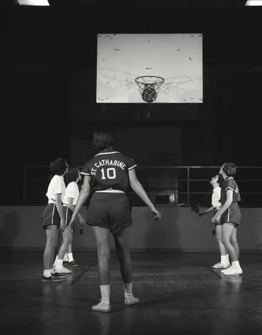 Vintage Photograph. Basket ball goes in hoop while players stand around free-throw perimeter.