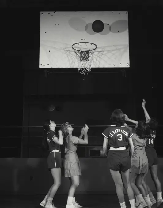 Vintage Photograph. Basketball is near hoop while female players are gathered underneath.