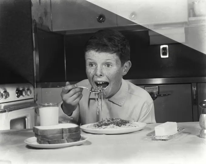 Vintage Photograph. Young boy puts a scoop of spaghetti into his mouth.