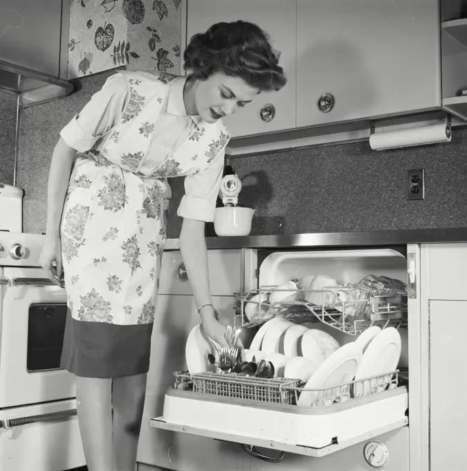 Vintage Photograph. Woman loads knives into dishwasher.