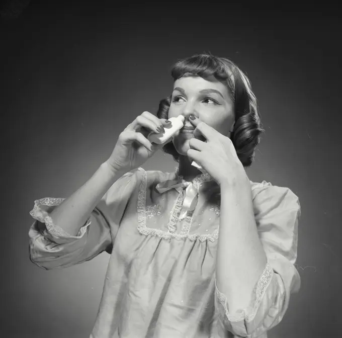 Vintage Photograph. Woman smiles while putting nose spray into her nose.