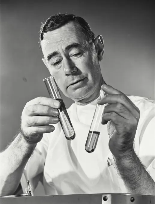 Vintage Photograph. Man in white coat looks at test tubes in studio portrait.