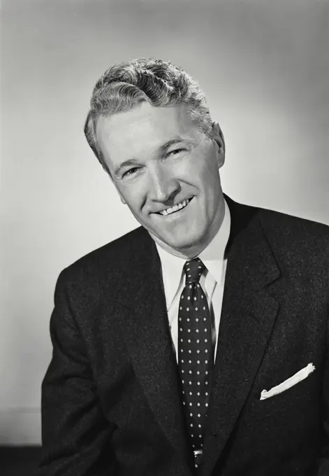 Vintage Photograph. Man smiles for studio portrait wearing business suit.