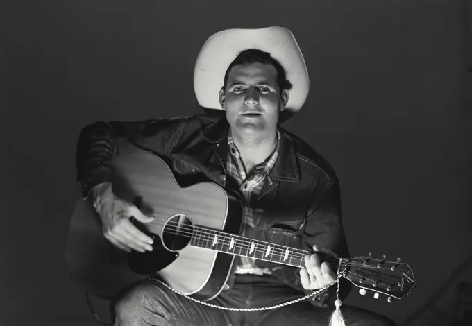 Vintage Photograph. Man sits playing guitar sings wearing cowboy hat.