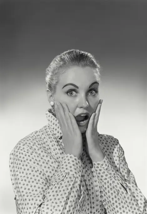 Vintage Photograph. Woman has a scared look on her face holding her cheeks with her hands.