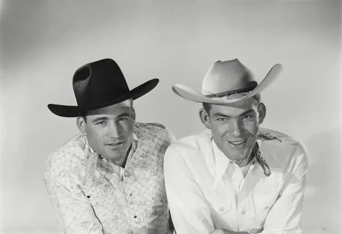 Vintage Photograph. Two men sit next to each other in studio portrait wearing cowboy hats one wears a bandana around neck.