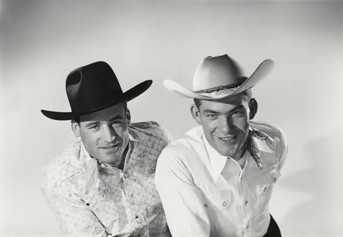 Vintage Photograph. Men sit next to each other in studio portrait wearing cowboy hats.