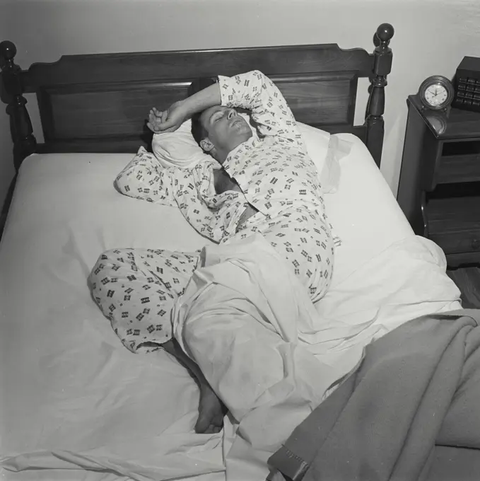 Vintage Photograph. Man lays in bed with fever he is not covered by the blankets.