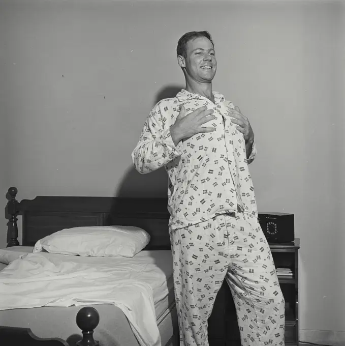 Vintage Photograph. Man stands next to bed touching breast he smiles.