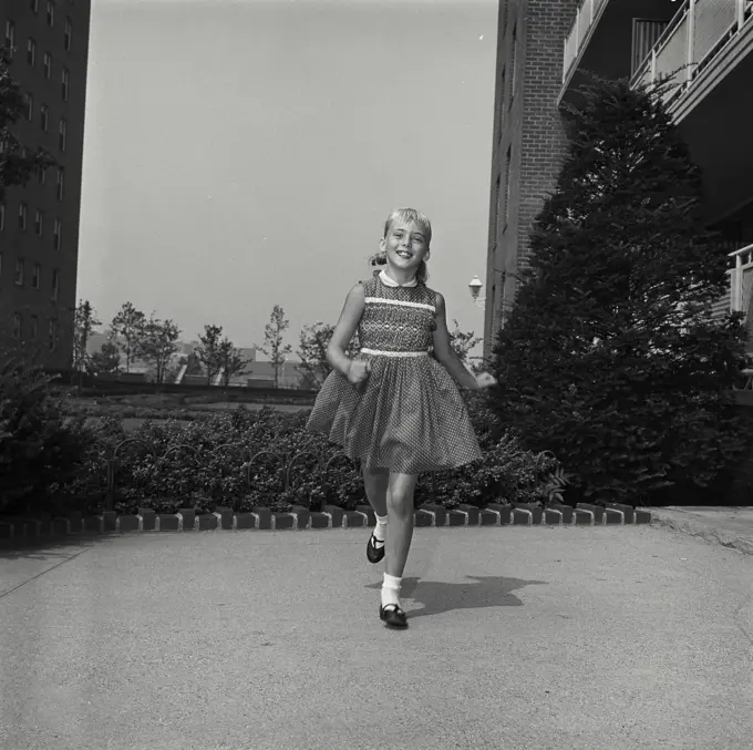 Vintage Photograph. Young girl smiles as she runs in apartment courtyard.