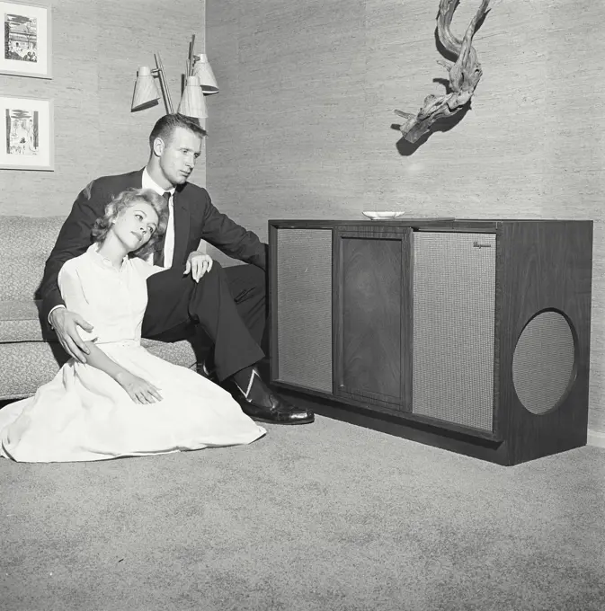 Vintage Photograph. Couple sits on couch looking over at music system.