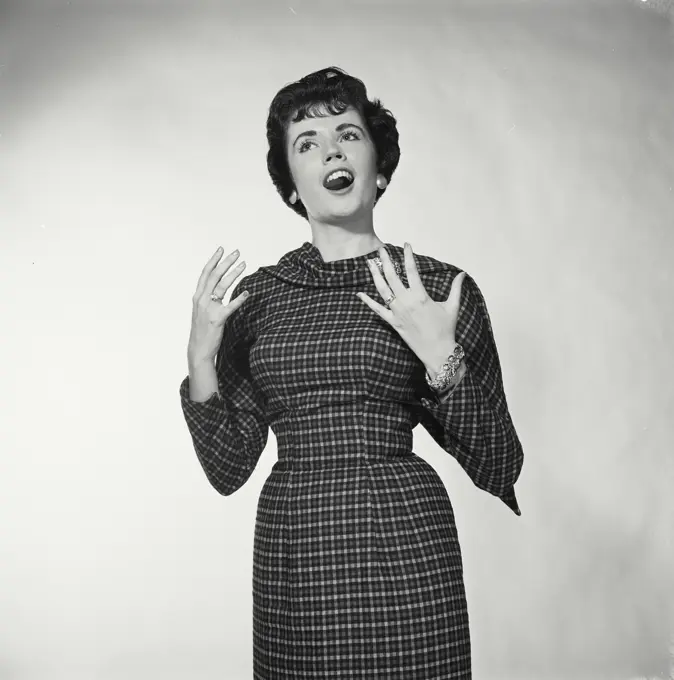 Vintage Photograph. Woman stands with her hands up singing she wears a checkered dress for studio portrait.