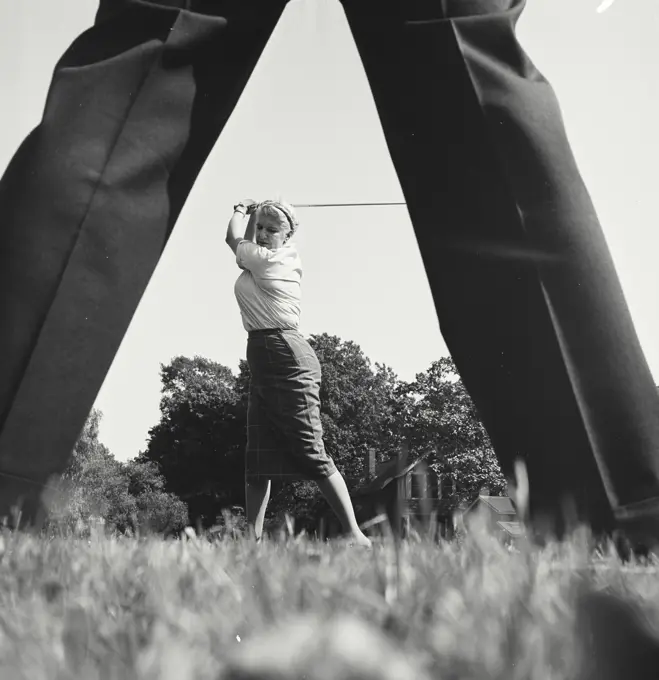 Vintage Photograph. Woman at top of swing of golf club between the legs of someone.