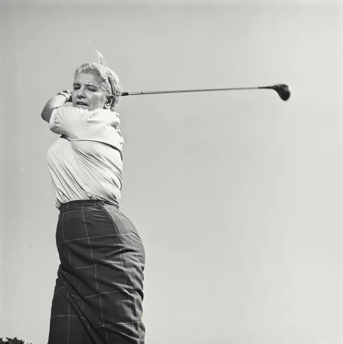 Vintage Photograph. Woman swings her golf club back as she looks to the ground.