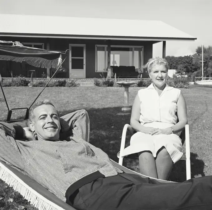 Vintage Photograph. Man relaxes in hammock while woman sits beside him.