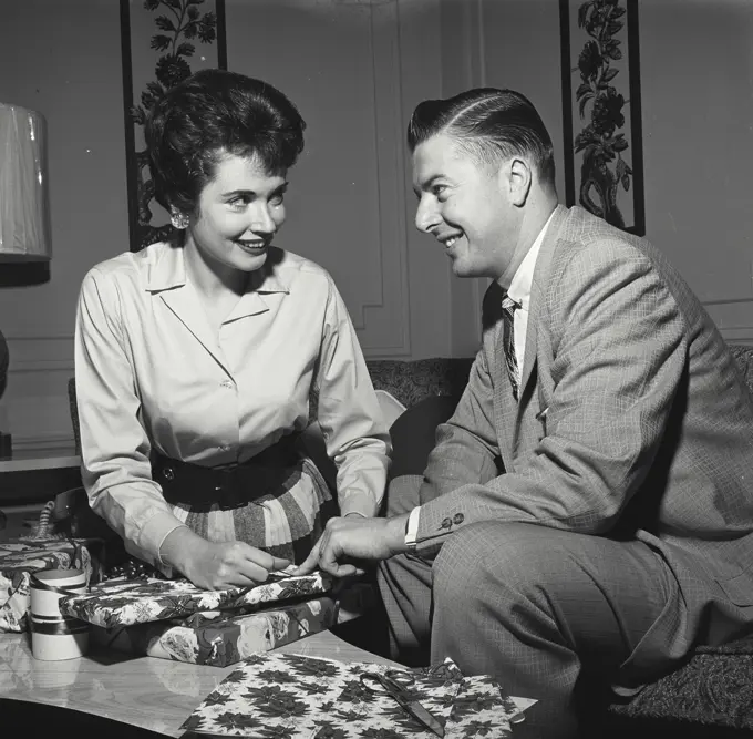 Vintage Photograph. Man and woman spend time in living room wrapping christmas gifts.