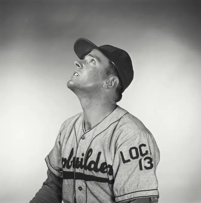 Vintage Photograph. Man sits for studio portrait looking up to the top left of frame wearing baseball uniform.