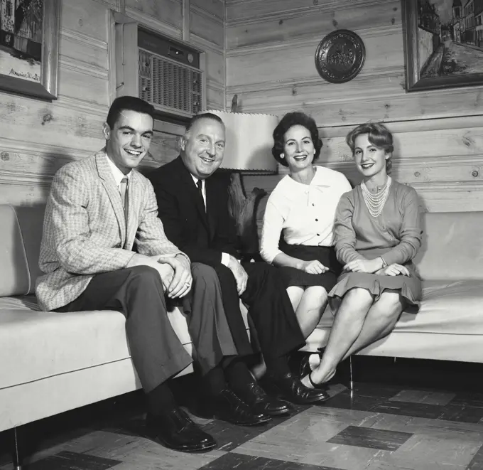 Vintage Photograph. Family sit together in living room on couches smiling.