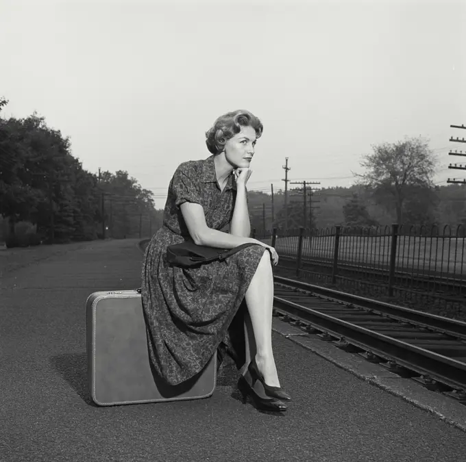 Vintage Photograph. Woman in dress sitting on suitcase.