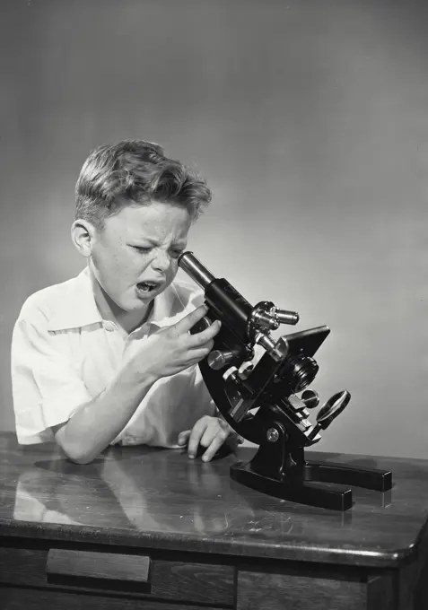 Vintage Photograph. young boy making funny expression looking into microscope on table