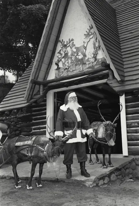 Vintage Photograph. Santa Claus standing with two reindeer in front of a building