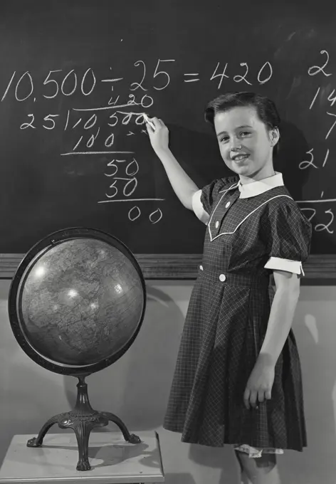 Vintage photograph. Young girl in dress writing on chalkboard