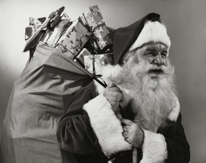 Side profile of Santa Claus carrying a sack of Christmas presents on his back