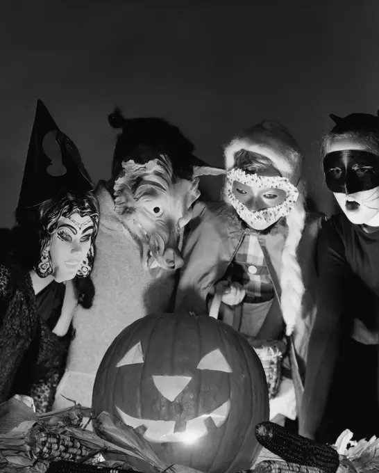 Four children wearing Halloween costumes looking at an illuminated jack o' lantern