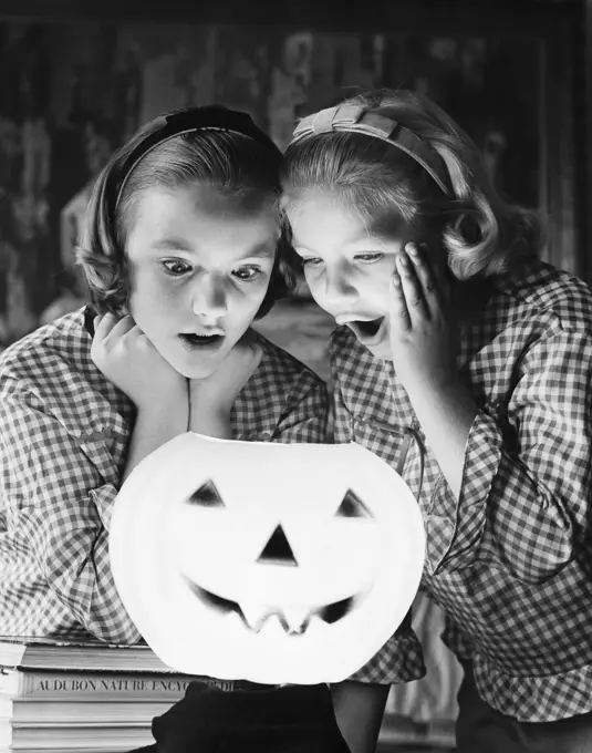 Close-up of two girls looking at an illuminated jack o' lantern