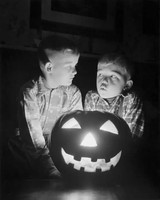 Two boys sitting behind an illuminated jack o' lantern